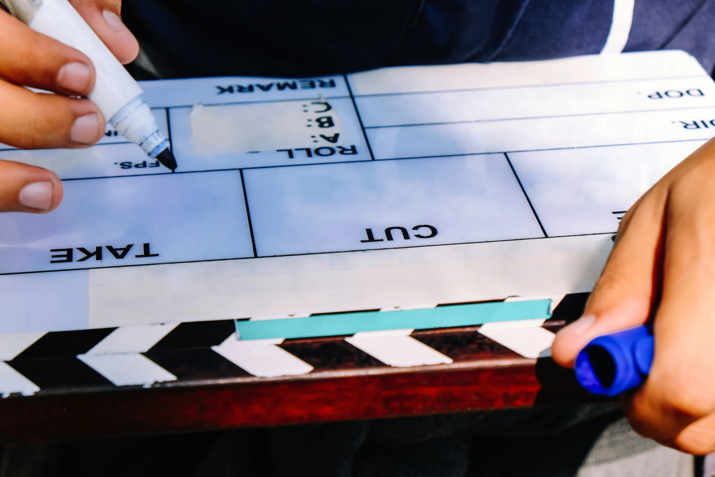 Close-up of a clapperboard marked Take and Cut, photographed as a crew member marks it in mirror reflection